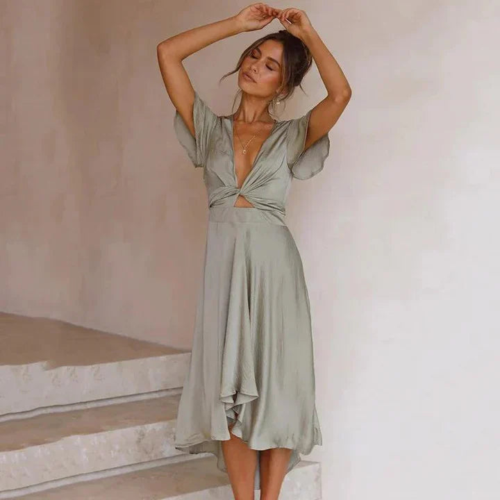 Frau in elegantem, fließendem, hellgrauem Kleid mit V-Ausschnitt und kurzen Ärmeln, posiert auf Treppe. Modetrend, Damenmode, Sommerkleid.