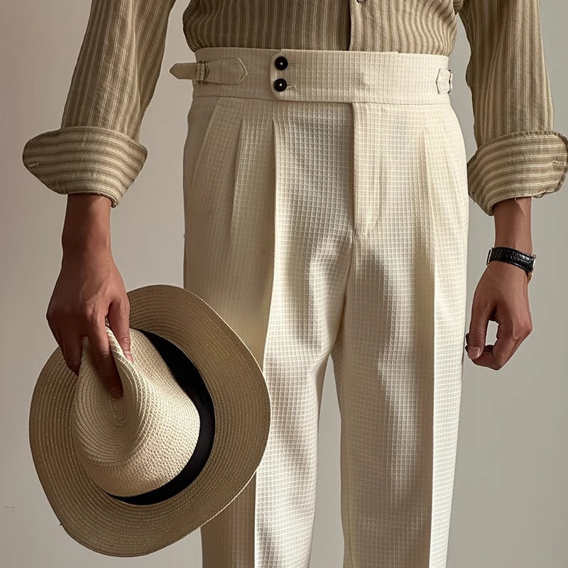 Eleganter Mann in cremefarbener Anzughose und gestreiftem Hemd hält einen Strohhut. Stilvolle Herrenmode, Vintage-Look, zeitloser Chic.