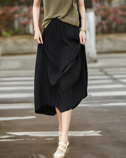 Frau in schwarzem, plissiertem Midirock und beigem Oberteil überquert Straße. Modetrend, Damenmode, eleganter Look, Straßenstil.