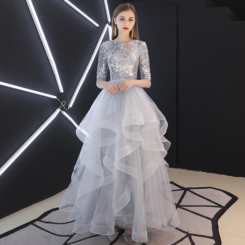 Elegantes Abendkleid mit silbernen Pailletten und voluminösem, mehrlagigem Tüllrock, getragen von einer Frau vor modernem, geometrischem Hintergrund.
