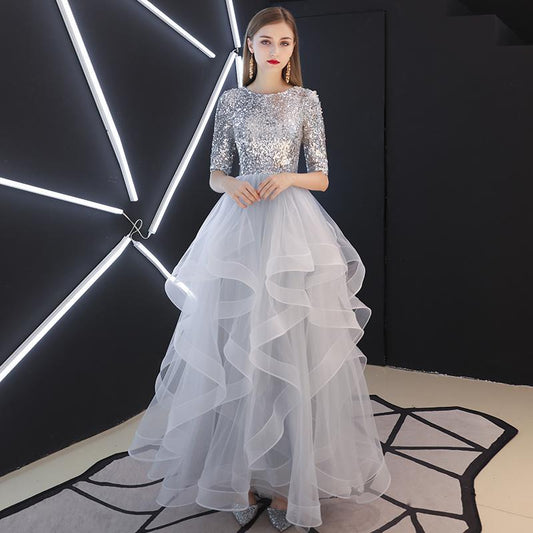 Elegantes Abendkleid mit silbernen Pailletten und voluminösem, mehrlagigem Tüllrock, getragen von einer Frau vor modernem, geometrischem Hintergrund.