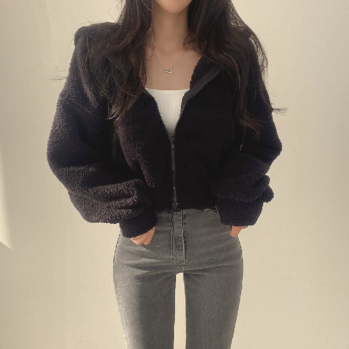 Frau in schwarzer Teddyjacke und grauer Jeans, modisch und lässig gekleidet, vor neutralem Hintergrund. Trendige Wintermode für Damen.
