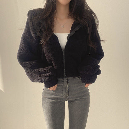 Frau in schwarzer Teddyjacke und grauer Jeans, modisch und lässig gekleidet, vor neutralem Hintergrund. Trendige Wintermode für Damen.