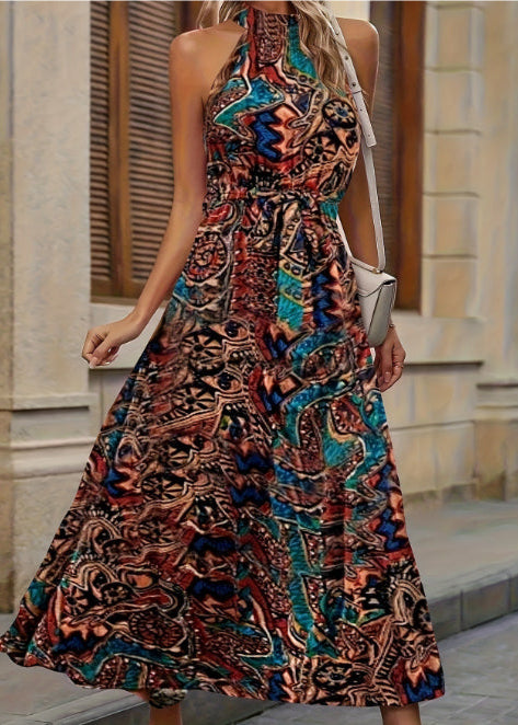 Frau in langem, ärmellosem Kleid mit buntem, abstraktem Muster, steht vor einer beigen Wand. Sommermode, Boho-Stil, elegantes Maxikleid.