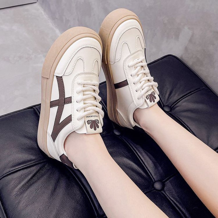Beige Sneaker mit braunen Details auf schwarzem Ledersessel, modische Damen-Sportschuhe, lässiger Stil, bequeme Freizeitschuhe für den Alltag.
