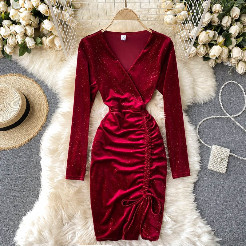 Rotes Samtkleid mit langen Ärmeln und Raffung, auf weißem Fellteppich, umgeben von weißen Rosen, Strohhut und Perlenhandtasche.