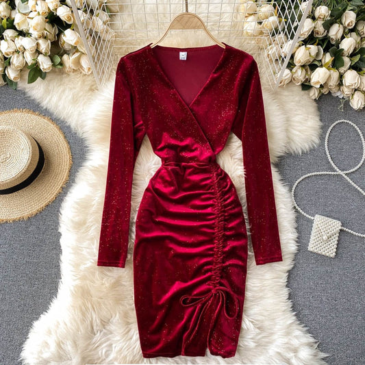 Rotes Samtkleid mit langen Ärmeln und Raffung, auf weißem Fellteppich, umgeben von weißen Rosen, Strohhut und Perlenhandtasche.