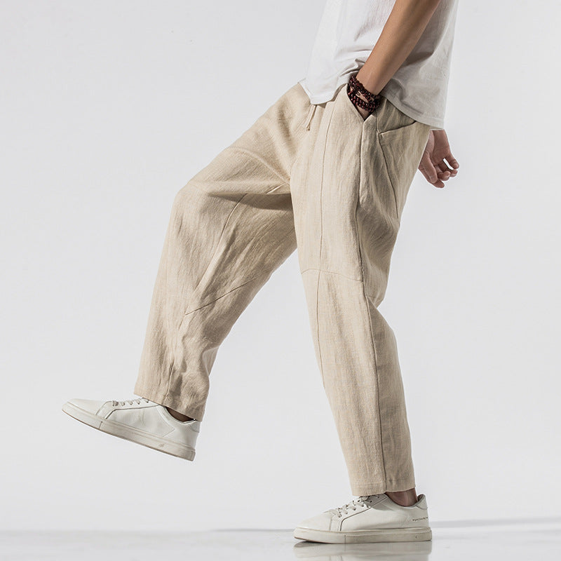 Beige Leinenhose für Herren, kombiniert mit weißen Sneakers und weißem T-Shirt. Lässiger, moderner Stil, ideal für Sommermode und Freizeitkleidung.