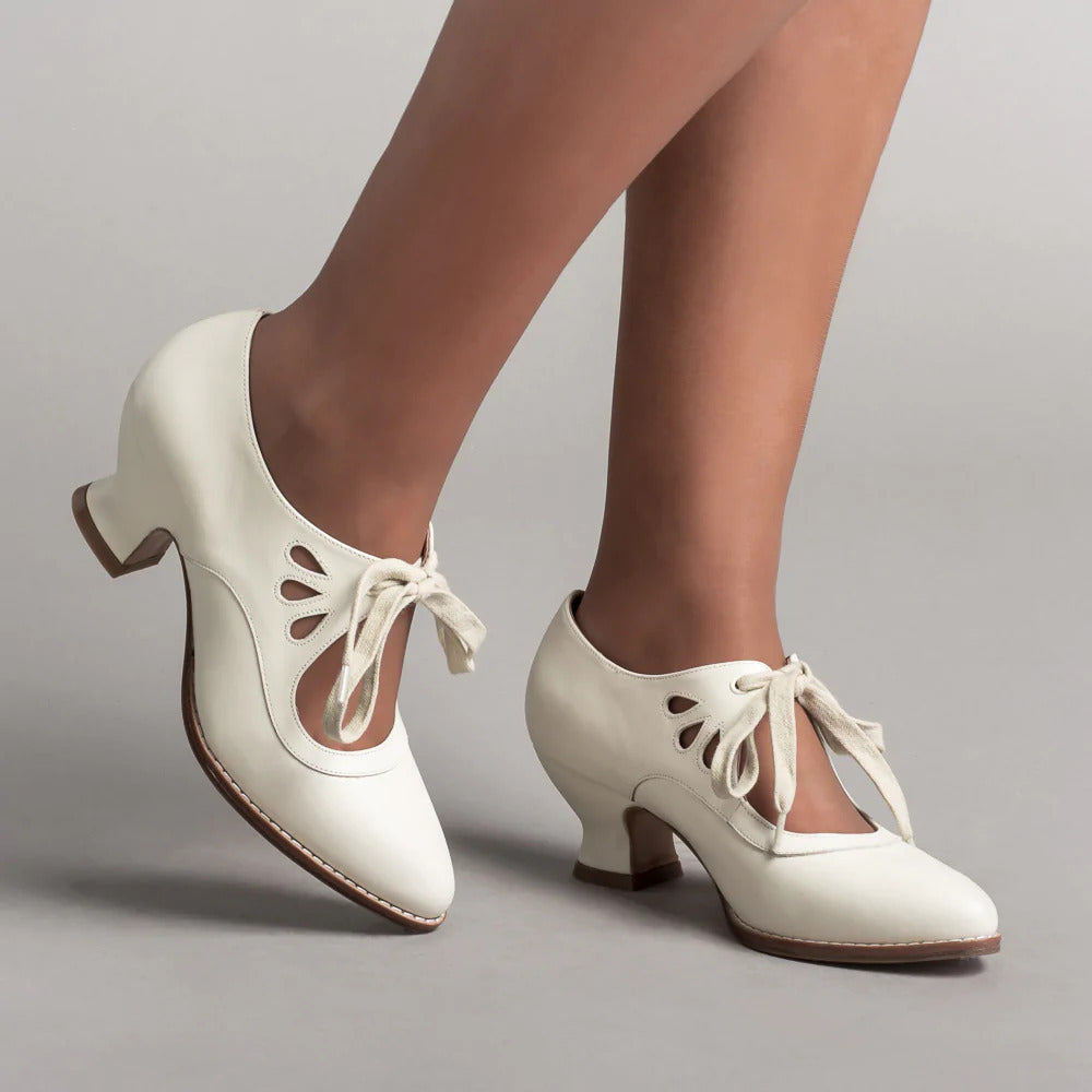 Weiße Vintage-Tanzschuhe mit niedrigen Absätzen und Schleifen, getragen von einer Person. Ideal für Swing, Lindy Hop und Retro-Mode-Enthusiasten.