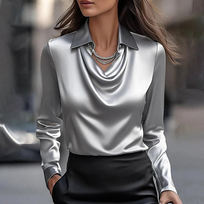 Frau in eleganter, silberner Satinbluse mit Kettenhalskette, modisch gekleidet, urbaner Hintergrund. Hochwertige Damenmode, stilvoller Look.