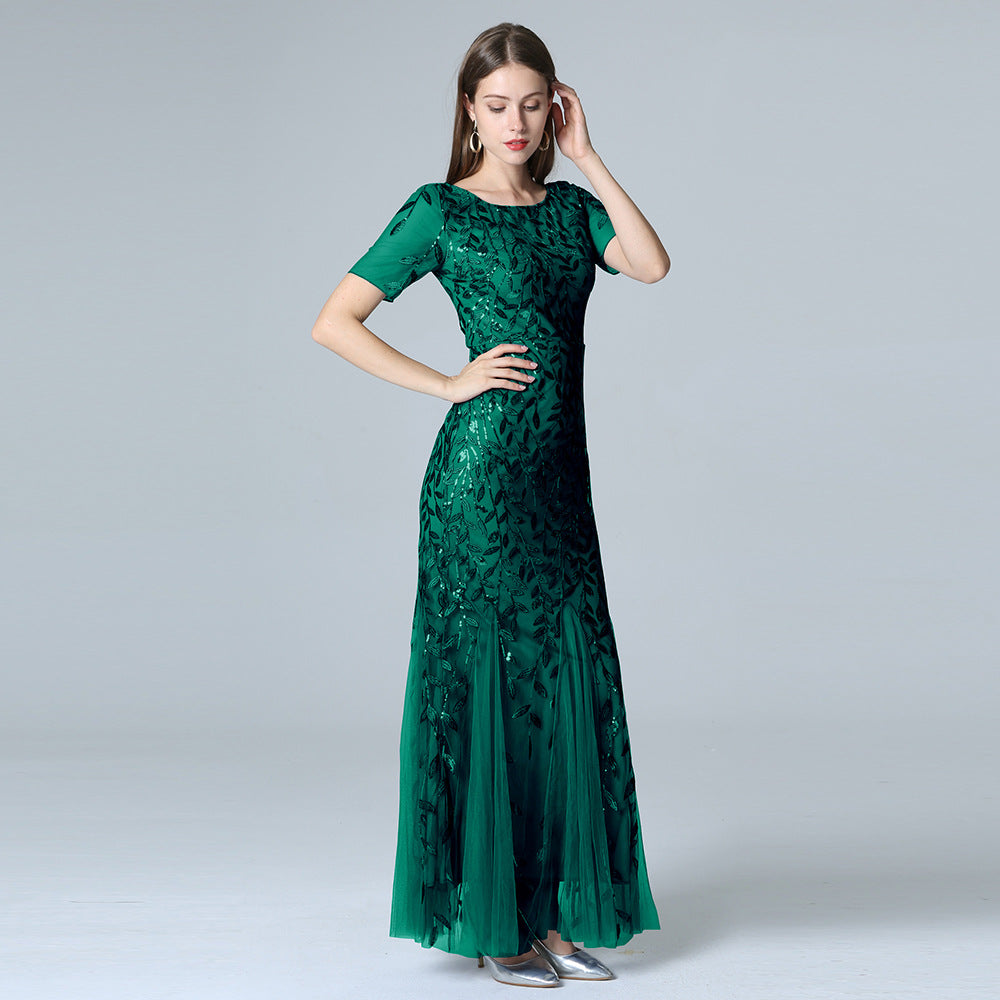 Frau in elegantem, grünem Abendkleid mit Pailletten, stehend vor grauem Hintergrund. Perfekt für formelle Anlässe und Mode-Events.