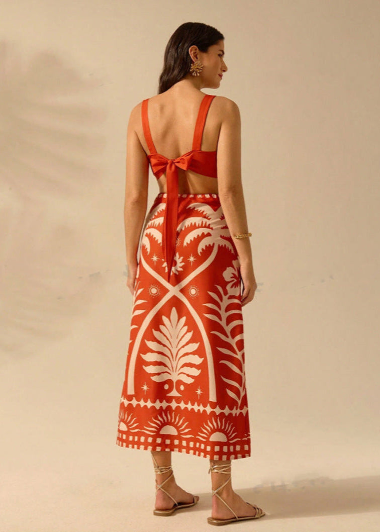 Frau in rotem, gemustertem Sommerkleid mit Schleife am Rücken, Sandalen, goldenen Ohrringen und Armband. Elegante Damenmode, Sommeroutfit.