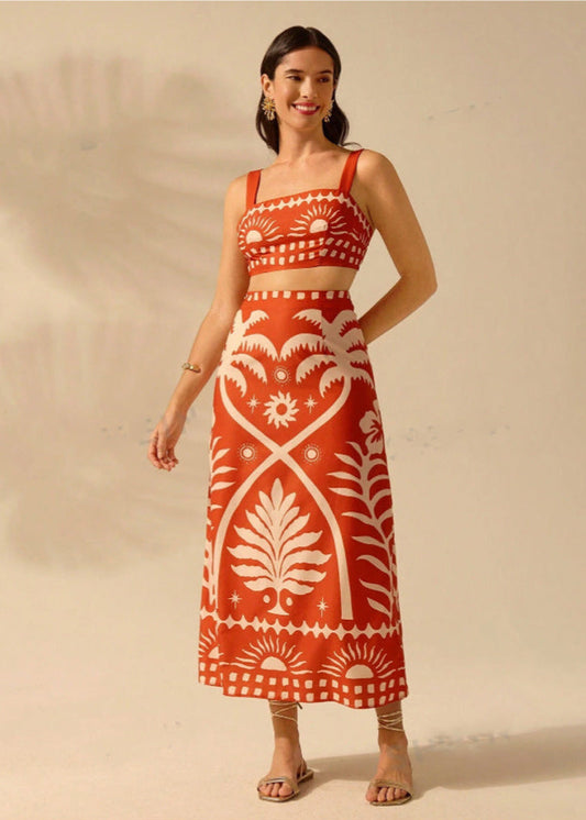 Frau in rotem, ärmellosem Kleid mit weißem, botanischem Muster, lächelt und trägt Sandalen. Elegante Sommermode, stilvolles Design.