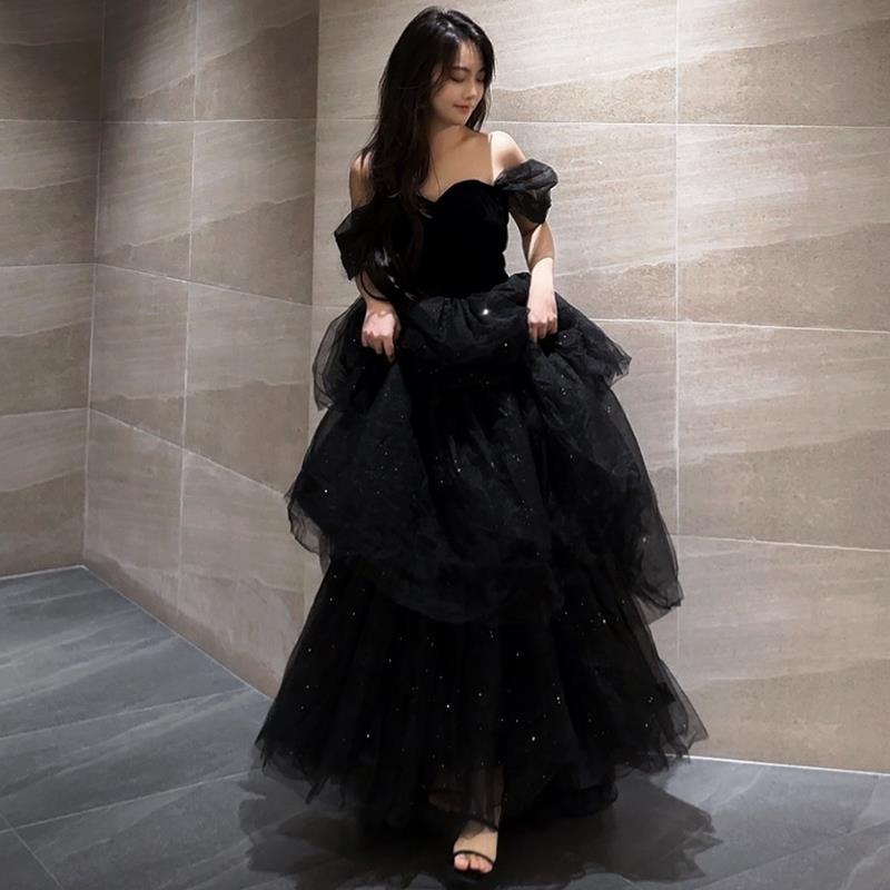 Frau in elegantem, schwarzem Abendkleid mit Tüll und Pailletten, steht in modernem, minimalistischem Raum. Abendmode, Ballkleid, Glamour.