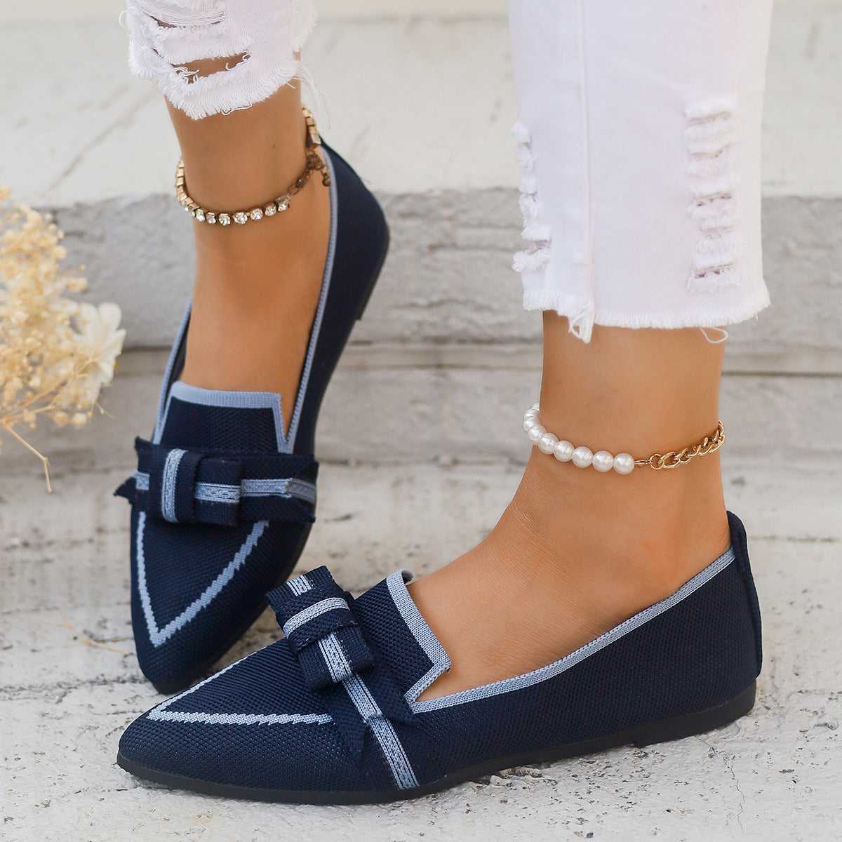 Damen tragen dunkelblaue Loafer mit Schleife und silbernen Details, kombiniert mit zerrissenen weißen Jeans und eleganten Fußkettchen.