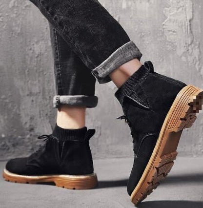 Schwarze Stiefeletten mit dicker Sohle, getragen von Person in hochgekrempelten Jeans, vor grauer Betonwand. Modische Damenstiefel, urbaner Stil.