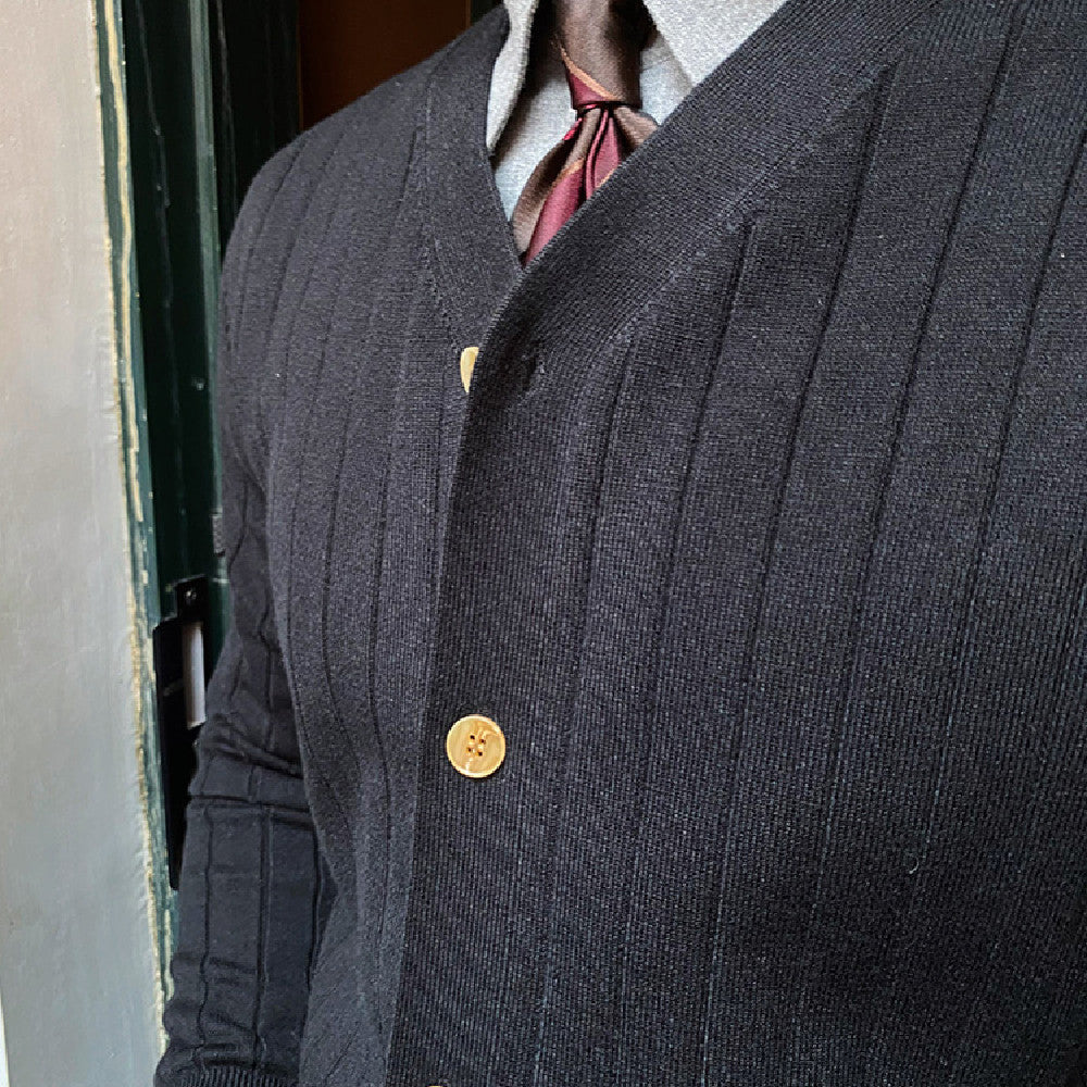 Eleganter schwarzer Strick-Cardigan mit goldenen Knöpfen, getragen über einem grauen Hemd und roter Krawatte. Herrenmode, stilvoll, klassisch.