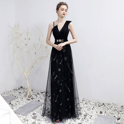 Elegantes schwarzes Abendkleid mit V-Ausschnitt und Gürtel, verziert mit Sternenmustern, getragen von einer Frau in einem minimalistischen Raum.