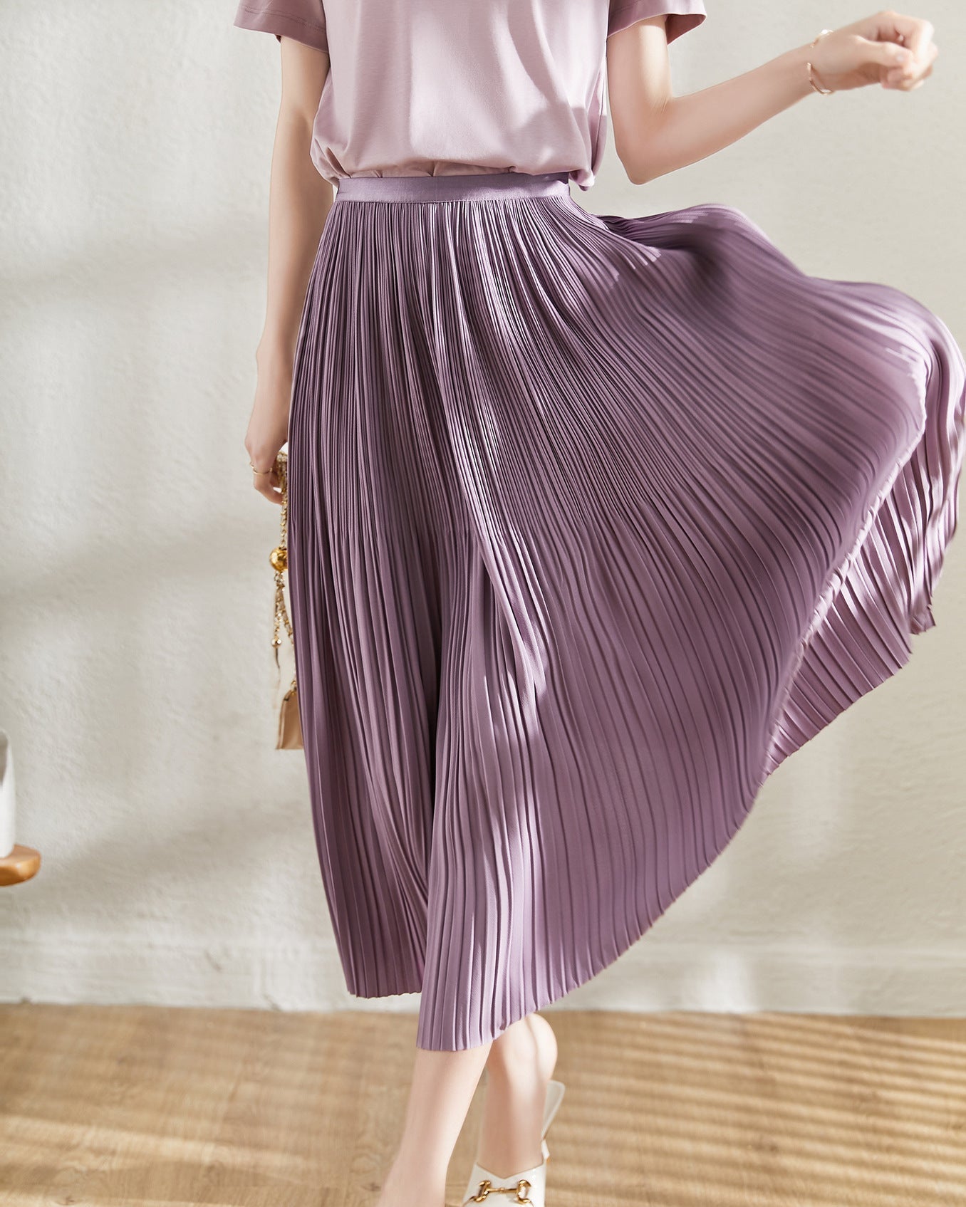 Frau in fliederfarbenem, plissiertem Midirock, schwingend, modisch, elegant, Sommermode, Innenraum, Holzboden, stilvoll, feminin.