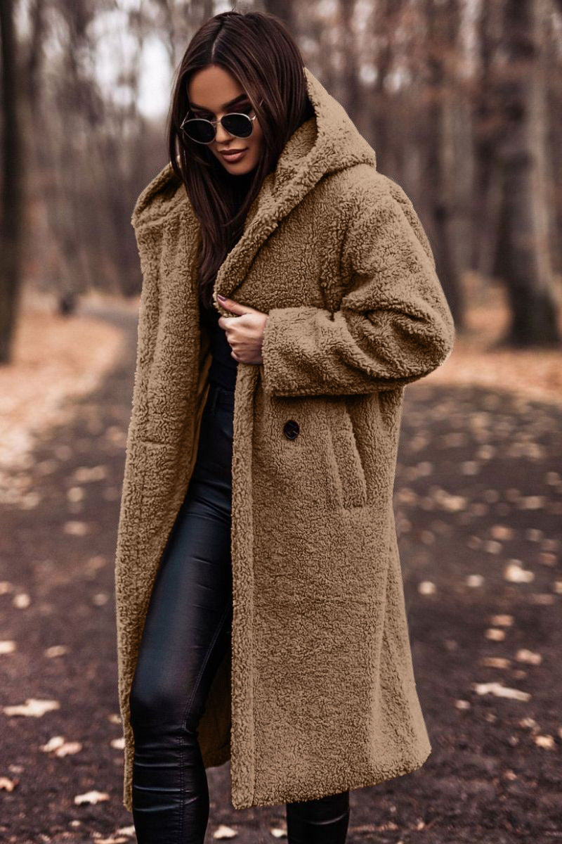 Frau im braunen Teddy-Mantel und Sonnenbrille spaziert im herbstlichen Wald. Modetrend, Herbstmode, stilvolle Damenbekleidung.