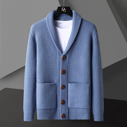 Blaue Strickjacke mit Schalkragen, Holzknöpfen und aufgesetzten Taschen, hängt auf einem Kleiderbügel vor grauem Hintergrund.