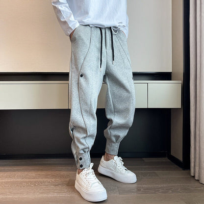 Mann in grauer Jogginghose und weißen Sneakers steht in modernem Raum. Bequeme Sportbekleidung, lässiger Stil, modische Freizeitmode.