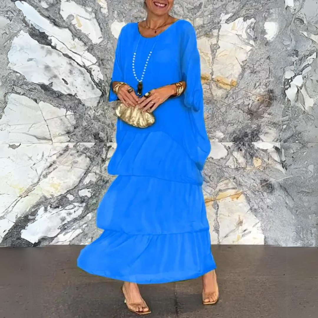 Frau in blauem Maxikleid vor marmorierter Wand, goldene Clutch, Perlenkette, elegante Sandalen. Mode, Damenbekleidung, Abendgarderobe.