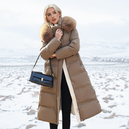 Frau in braunem Daunenmantel mit Pelzkragen, schwarze Handtasche, schneebedeckte Landschaft im Hintergrund. Wintermode, stilvoll, elegant.