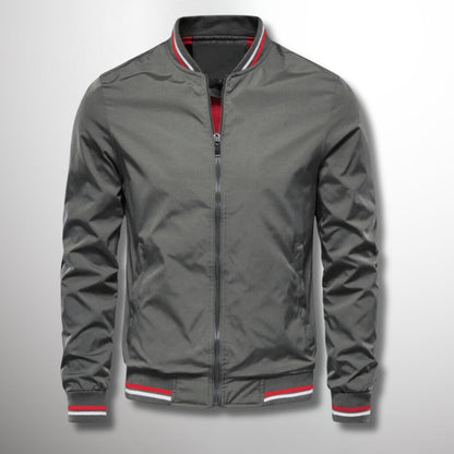 Graue Bomberjacke mit Reißverschluss, roten und weißen Streifen an Kragen und Bündchen, modisch und vielseitig für Herrenmode.