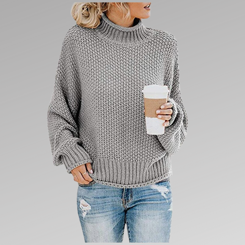Frau in grauem Strickpullover hält Kaffeebecher, trägt zerrissene Jeans. Modetrend, Herbstmode, lässiger Stil, gemütlicher Look.