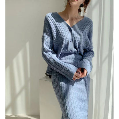 Frau in hellblauem Strickset mit V-Ausschnitt und Knöpfen, bestehend aus Pullover und Rock, steht in hellem Raum. Modetrend, Damenmode, Strickkleidung.