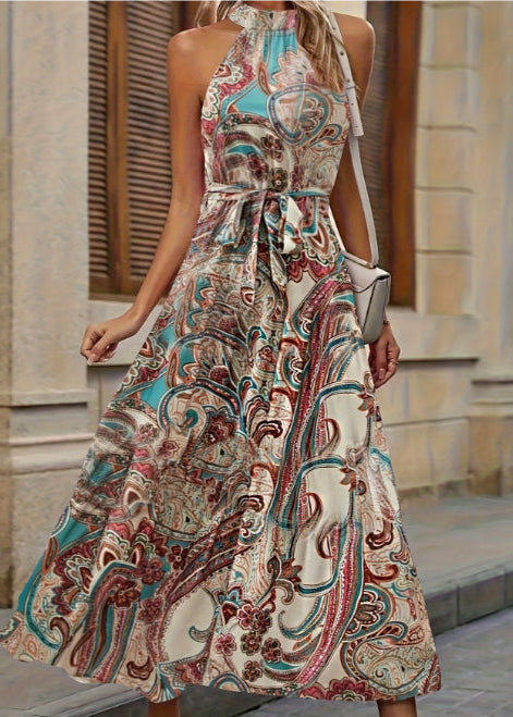 Frau in langem, ärmellosem Kleid mit buntem Paisley-Muster, steht auf einer städtischen Straße. Elegantes Sommeroutfit, modisches Design.