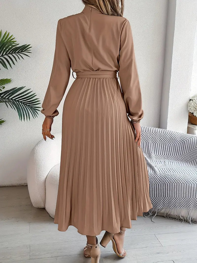 Frau in elegantem, langem, beigem Plisseekleid, steht in modernem Wohnzimmer. Stilvolle Mode, Herbstkleid, Damenbekleidung, schickes Design.