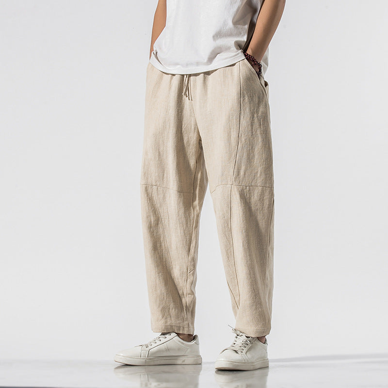 Beige Leinenhose für Herren, lässig geschnitten, kombiniert mit weißem T-Shirt und Sneakers. Ideal für Sommermode und Freizeitkleidung.