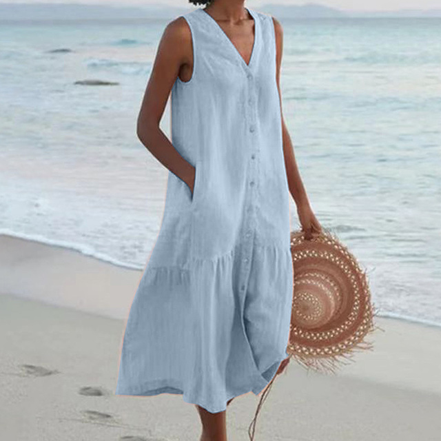 Frau in hellblauem Sommerkleid am Strand, hält runden Strohhut. Strandmode, Sommerkleid, Damenbekleidung, Strandspaziergang.