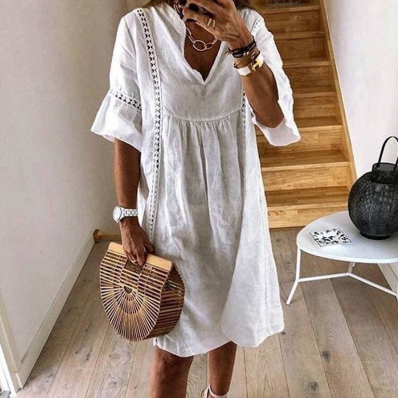 Frau in weißem Leinenkleid mit Holzhandtasche, modisch, Sommermode, Treppe im Hintergrund, stilvoll, lässig, Accessoires, Innenraum.