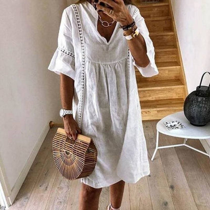 Frau in weißem Leinenkleid mit Holzhandtasche, modisch, Sommermode, Treppe im Hintergrund, stilvoll, lässig, Accessoires, Innenraum.
