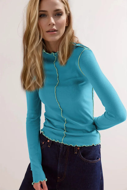 Blonde Frau in blauem Langarmshirt mit Rüschen, kombiniert mit dunkelblauer Jeans. Modetrend, Damenbekleidung, stilvolles Outfit.