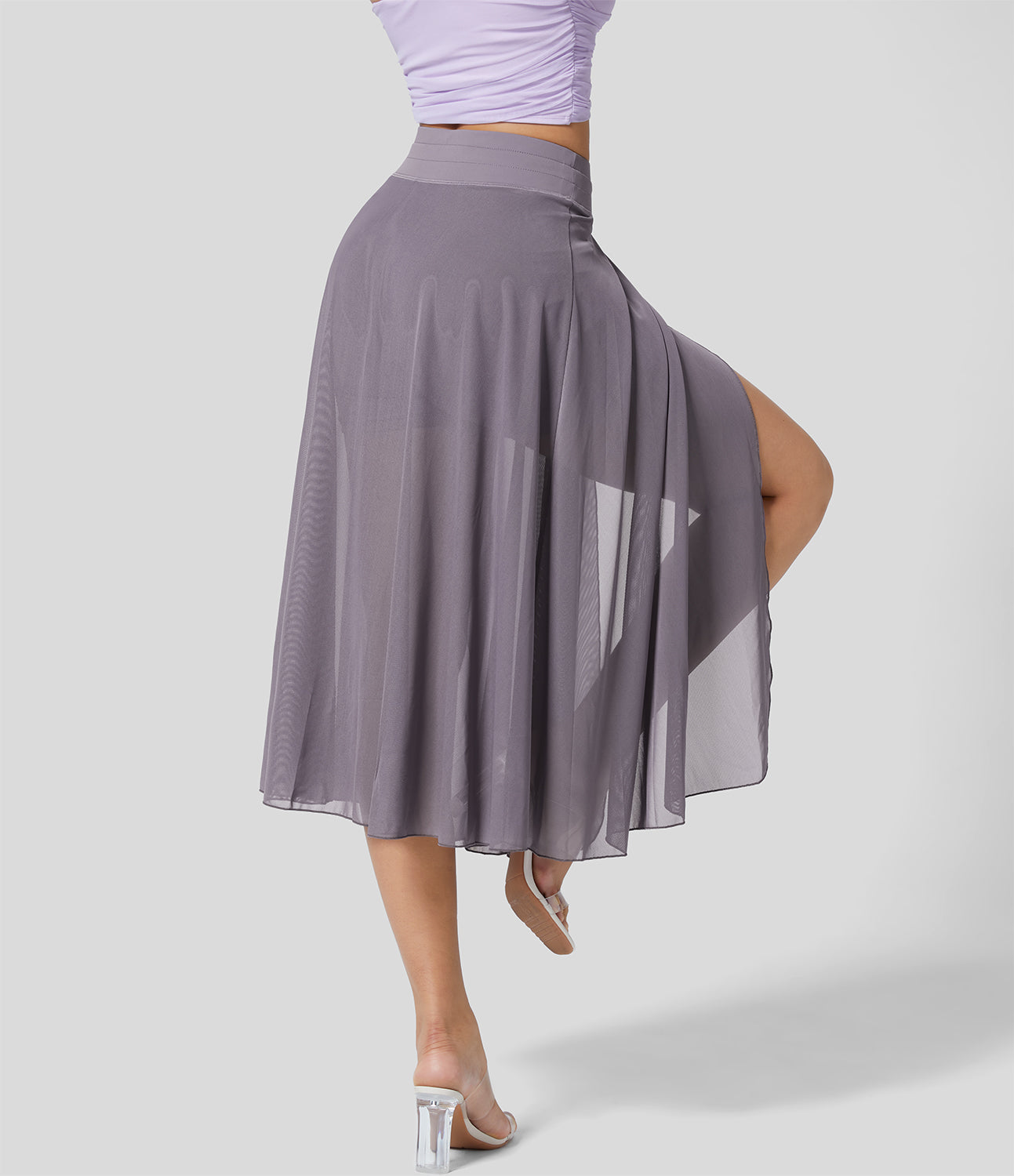 Frau in lila Tanzrock aus Chiffon, zeigt Beinpose. Eleganter, fließender Stoff, ideal für Ballett und Tanz. Transparentes Design, moderner Stil.