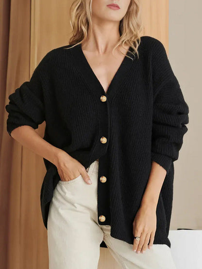 Frau trägt schwarzen Strick-Cardigan mit goldenen Knöpfen, kombiniert mit beigen Hosen. Modetrend, Herbstmode, Damenbekleidung.