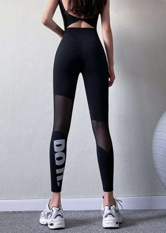 Frau in schwarzer Sportleggings mit Mesh-Einsätzen und Schriftzug, von hinten fotografiert, trägt weiße Turnschuhe. Fitnessmode, Sportbekleidung.