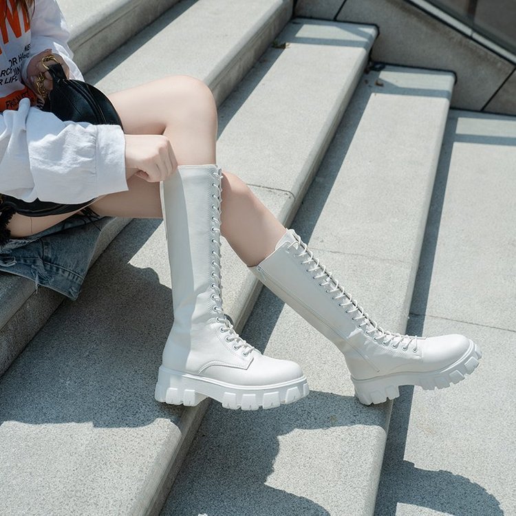 Weiße kniehohe Stiefel mit Schnürung auf Treppe, modisch und trendig. Perfekt für Herbstmode und Streetstyle. Damenstiefel, urbaner Look.