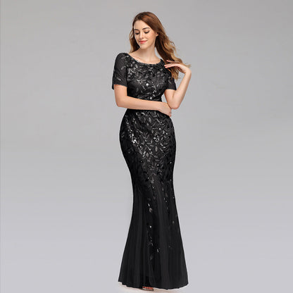 Frau in elegantem, schwarzem Abendkleid mit Pailletten, lächelt und posiert vor grauem Hintergrund. Perfekt für Gala, Ball oder Abendveranstaltung.