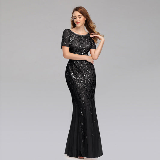 Frau in elegantem, schwarzem Abendkleid mit Pailletten, lächelt und posiert vor grauem Hintergrund. Perfekt für Gala, Ball oder Abendveranstaltung.