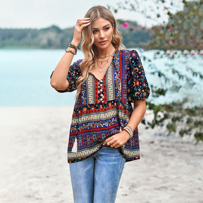 Frau in bunter Boho-Bluse und Jeans am Strand, umgeben von Natur. Sommermode, Freizeitkleidung, Strandoutfit, Boho-Stil.