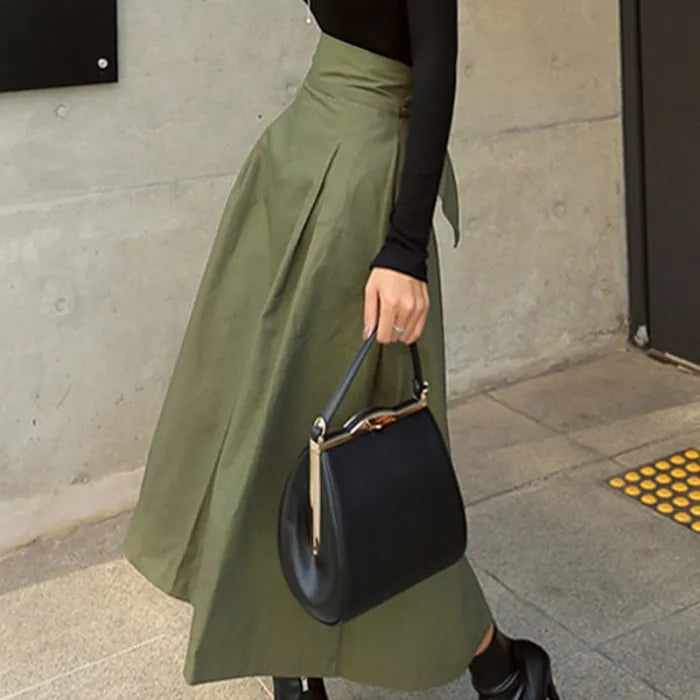 Frau in olivgrünem Midirock und schwarzem Oberteil trägt schwarze Handtasche. Modetrend, eleganter Streetstyle, Herbstmode.