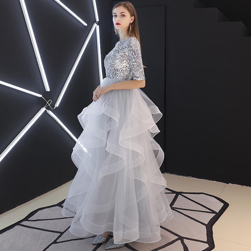 Frau in silbernem Paillettenkleid mit voluminösem, mehrlagigem Tüllrock, steht vor moderner, geometrischer LED-Beleuchtung. Elegantes Abendmode-Foto.