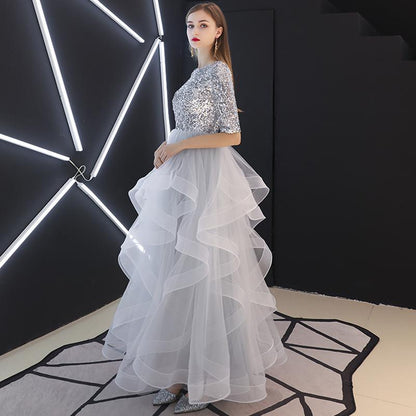 Frau in silbernem Paillettenkleid mit voluminösem, mehrlagigem Tüllrock, steht vor moderner, geometrischer LED-Beleuchtung. Elegantes Abendmode-Foto.