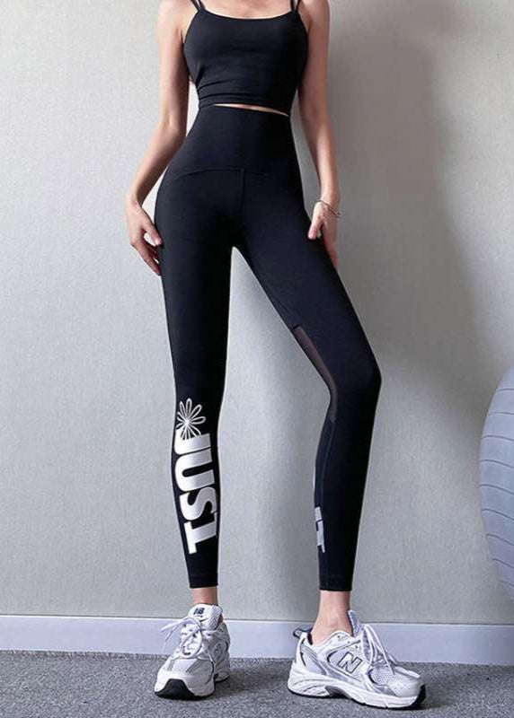 Frau in schwarzem Sport-BH und Leggings mit "USA"-Aufdruck, trägt weiße Turnschuhe. Fitnessmode, Sportbekleidung, athletischer Look.