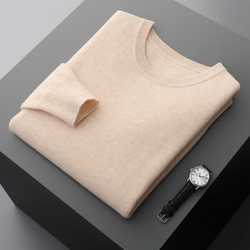 Beigefarbener Kaschmirpullover auf grauem Tisch, daneben eine elegante Armbanduhr mit schwarzem Lederarmband und weißem Zifferblatt.